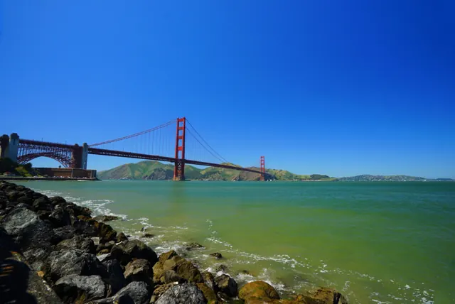 The Golden Gate Bridge across green water on a clear blue day