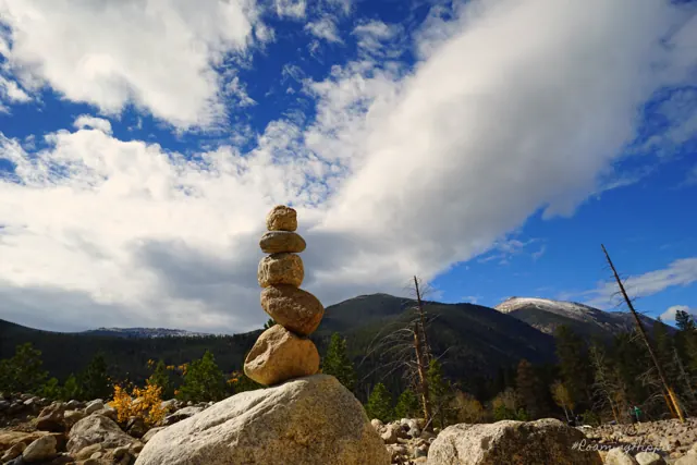 A stone cairn on a boulder with mountains and clouds behind