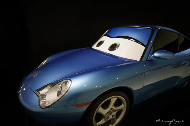A blue Porsche painted with cartoon eyes in a dark museum