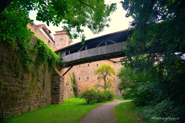 A covered wooden bridge crossing between stone walls among trees