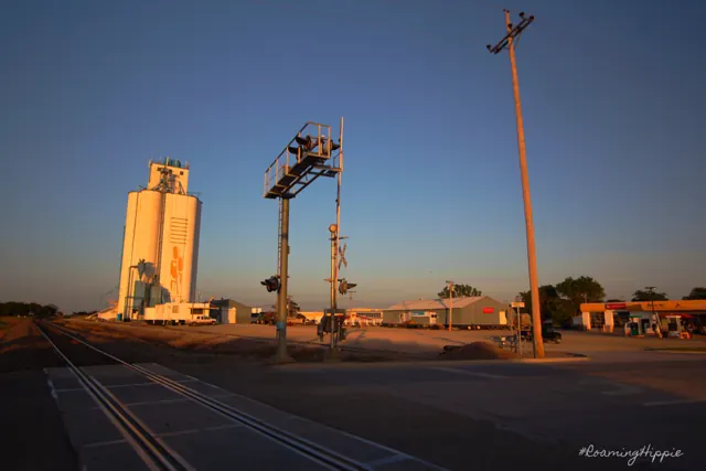 A white grain elevator and railroad signals at dusk