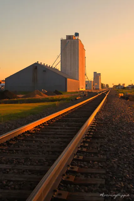 Railroad tracks leading to a grain elevator at sunset