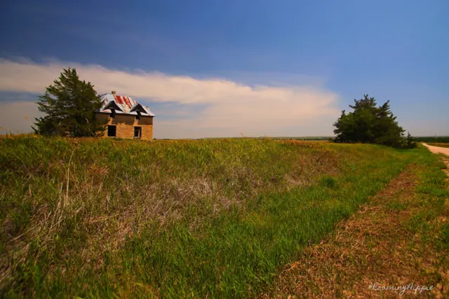 A distant farmhouse on a green rise under a wide sky