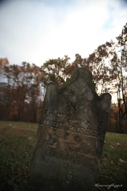 A tall, worn gravestone against autumn trees