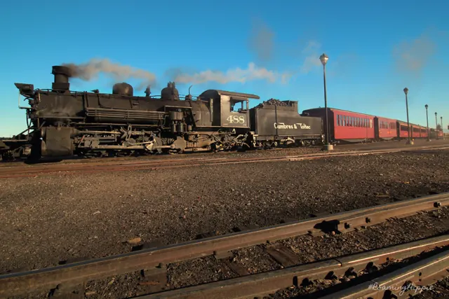 A steam locomotive and red passenger cars at a station