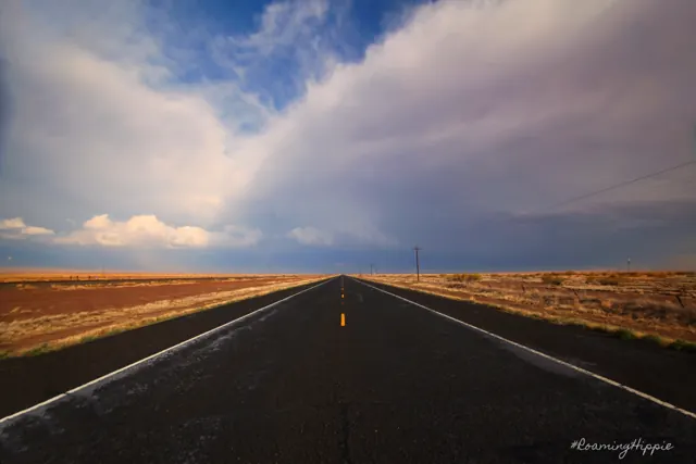 A straight two-lane highway running to the horizon under a sweep of white cloud