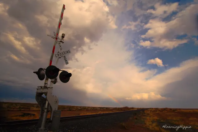 A railroad crossing signal against towering clouds over open prairie