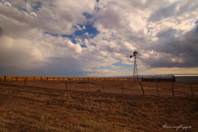 A windmill and a long freight train crossing flat grassland under heavy clouds