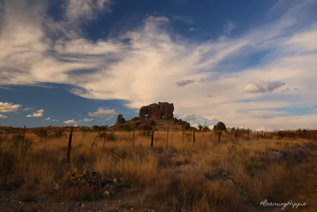 A lone rock outcrop on golden grassland under wispy clouds