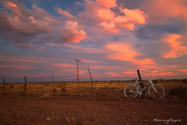 A white bicycle propped against a fence under a pink sunset sky