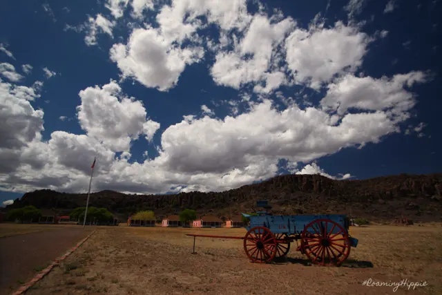 An old red wagon in front of rocky hills and puffy white clouds