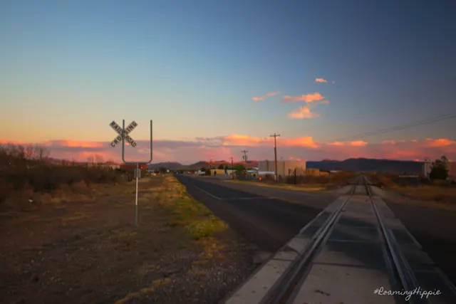 A railroad crossing and road at dusk under a pastel sky