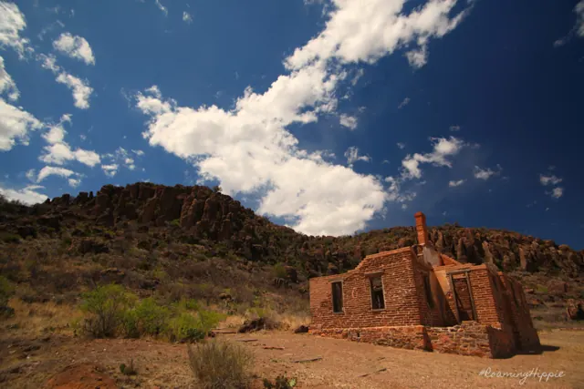 Crumbling adobe ruins below a rocky ridge under a blue sky